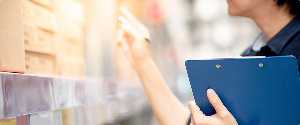 クリップボードを持って棚の商品を確認するスタッフ